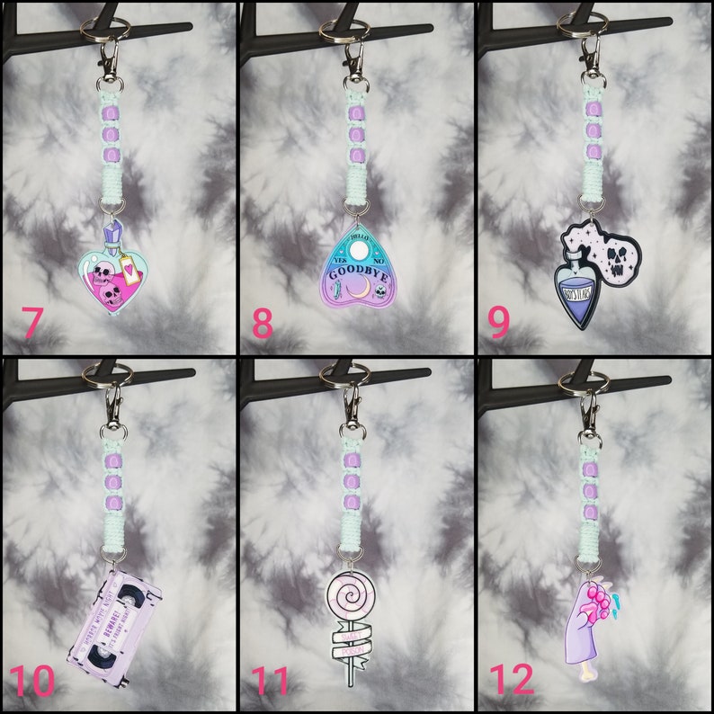 May include: Set of 6 keychains with different charms, including a potion bottle, a Ouija board, a skull, a cassette tape, a lollipop, and a hand holding a bouquet of flowers. Each charm is attached to a light blue and purple beaded chain.