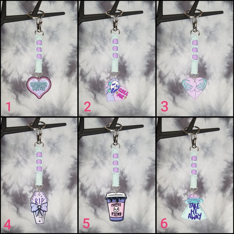 May include: Six different keychain charms with a pastel color scheme. The charms are attached to a light blue and purple beaded keychain. The charms include a heart with the text "Horror Hottie", a ghost with the text "Call Me", a heart with two hands, a coffin with the text "RIP", a coffee cup with the text "Coffee Fiend", and a UFO with the text "Take Me Away".