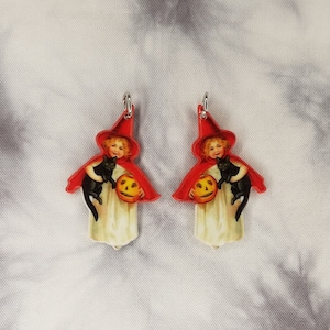 May include: A pair of Halloween-themed earrings featuring a vintage illustration of a girl dressed as a witch holding a black cat and a jack-o'-lantern.