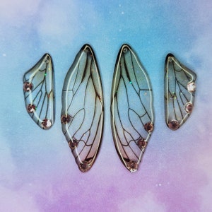 Puede incluir: Cuatro pendientes iridiscentes, transl&uacute;cidos, en forma de ala de mariposa con un delicado y complejo patr&oacute;n de venas. Los pendientes son de color azul claro con un ligero brillo.