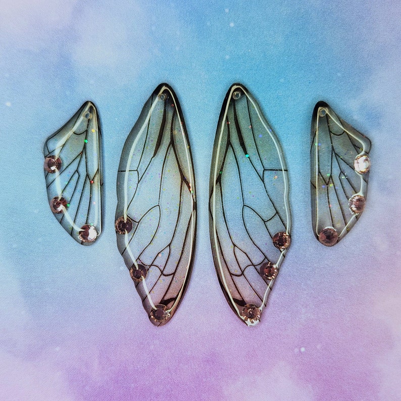 Puede incluir: Cuatro pendientes iridiscentes, transl&uacute;cidos, en forma de ala de mariposa con un delicado y complejo patr&oacute;n de venas. Los pendientes son de color azul claro con un ligero brillo.