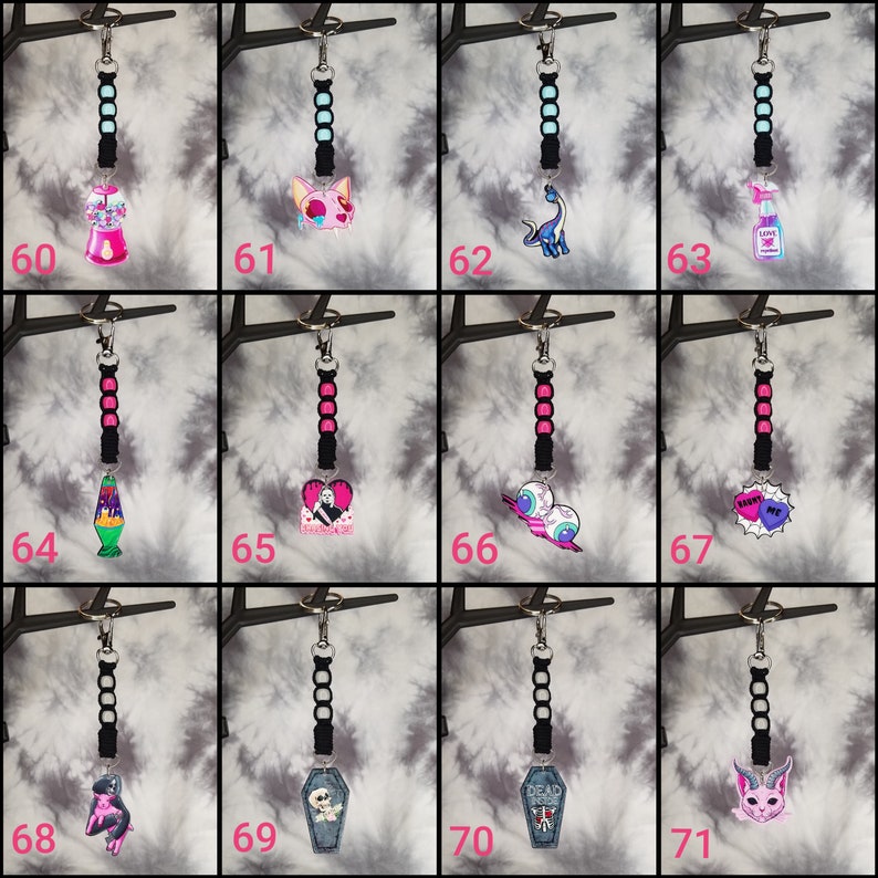 May include: A set of 12 keychains with various colorful cartoon designs. Each keychain features a black beaded strap and a silver key ring. The designs include a lava lamp, a cat, a dinosaur, a bottle of hand sanitizer, a cactus, a heart with a skull, a pair of eyes, a heart with the words "Swoon Me", a pink creature, a coffin, a coffin with the words "Dead Inside", and a pink cat.