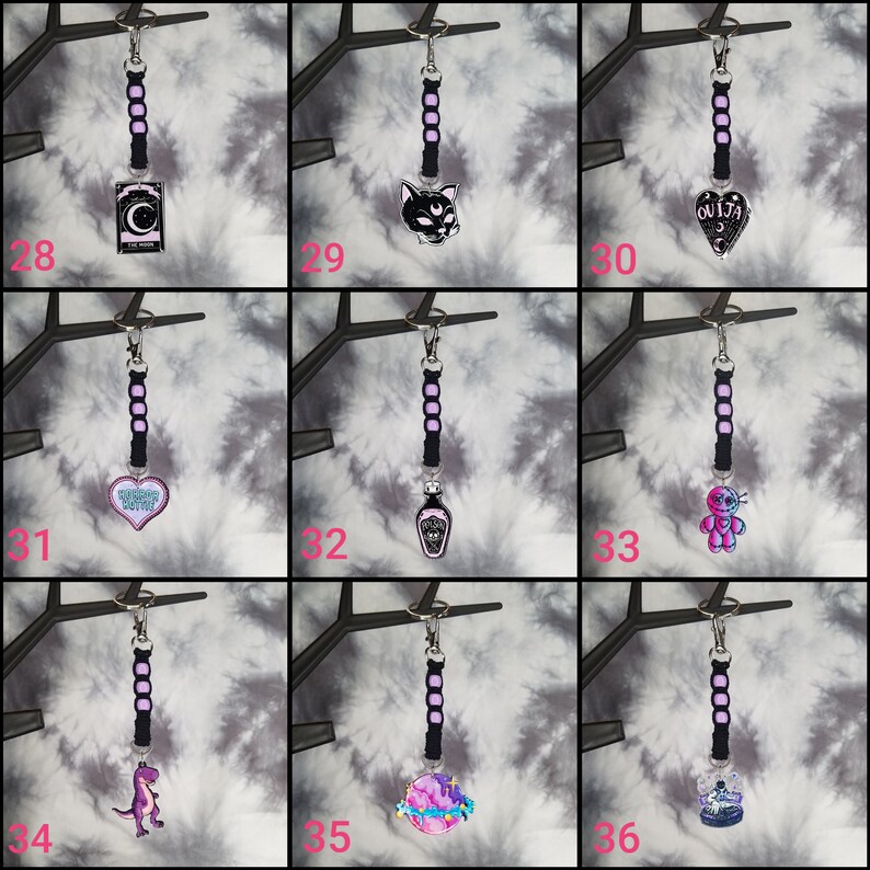 May include: Nine black keychains with different charms. The charms include a crescent moon, a black cat, a heart with the text "Greatest Love Story", a potion bottle, a voodoo doll, a dinosaur, a planet, a skull, and a heart with the text "Ouija".