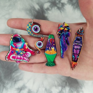 May include: Six colorful keychains featuring various designs, including an astronaut, a lava lamp, an octopus, and mushrooms. The keychains are made of acrylic and have a glossy finish.