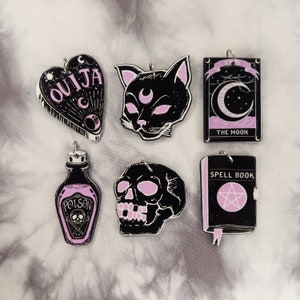 May include: Six black and pink charms with a spooky theme. The charms include a Ouija board, a cat, a crescent moon, a skull, a potion bottle, and a spell book.