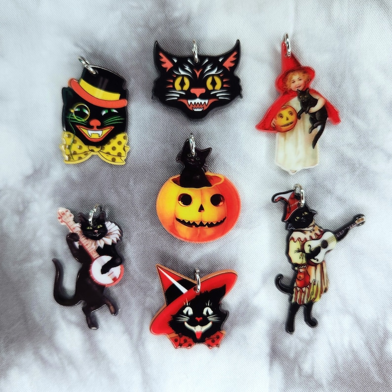May include: Set of seven Halloween-themed charms featuring black cats, pumpkins, and a witch. The charms are made of plastic and have a vintage look.