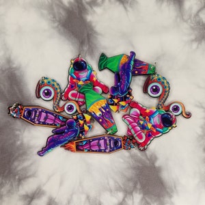 May include: A set of six colorful astronaut and alien themed keychains. The keychains are made of wood and feature intricate details. The keychains are painted in a variety of bright colors, including pink, purple, green, blue, and yellow.