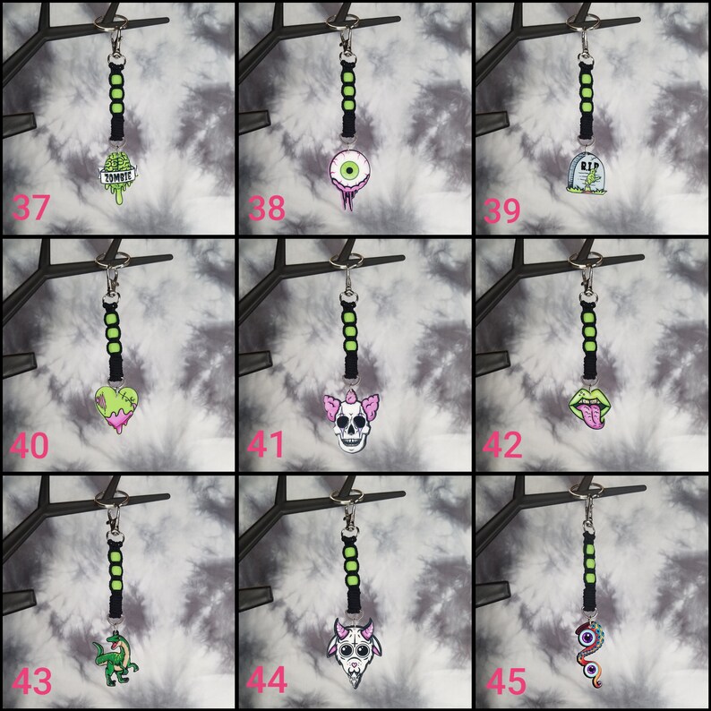 May include: A set of 9 keychains with black and green string and various colorful charms. The charms include a zombie ice cream cone, an eyeball, a tombstone, a bleeding heart, a skull, a tongue, a dinosaur, a goat, and a snake.