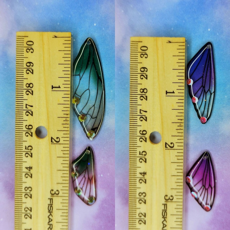 Puede incluir: Dos pares de alas iridiscentes con un dise&ntilde;o transl&uacute;cido y en capas. Un par es azul y morado, el otro es verde y azul. Las alas miden aproximadamente 5 cm de largo y se miden con una regla.