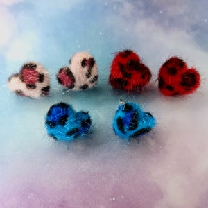 May include: Six fuzzy heart-shaped earrings in various colours, including pink, red, and blue. Each earring has a black and white leopard print pattern.