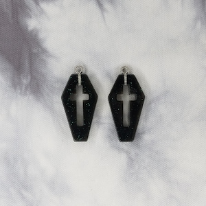 May include: A pair of black coffin-shaped earrings with a silver cross cutout and glitter accents.