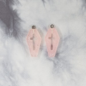 May include: A pair of pink glitter coffin-shaped earrings with a silver cross cutout.