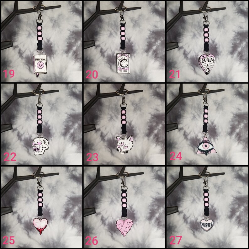 May include: Nine black and pink keychains with different charms. The charms include a skull, a cat, a heart, a book, a tarot card, a Ouija board, a triangle with an eye, and a heart with the word "murder".