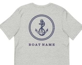 May include: A light gray t-shirt featuring a navy blue nautical design on the back. The design includes an anchor inside a rope circle, with the text "BOAT NAME" below. The shirt is made of a soft material.
