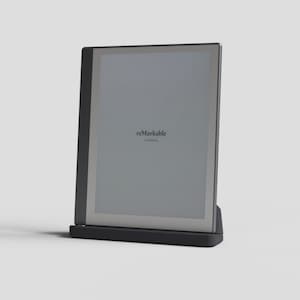 May include: A black e-reader device with a gray screen displaying the text "reMarkable is sleeping." The device is propped up on a black stand. The screen has a gray border.