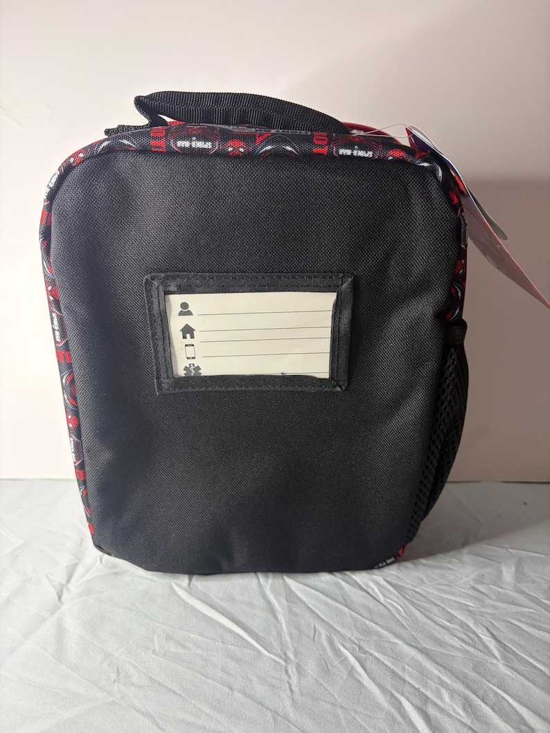 May include: Black lunch bag featuring a red and black Spider-Man pattern around the top and handle. It has a small clear window for a name tag. A black mesh pocket is on the side.
