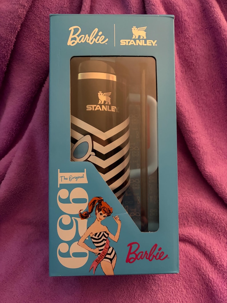 Puede incluir: Un juego en caja que presenta un termo Stanley en blanco y negro y una taza a juego, ambos con el logotipo de Stanley. La caja es azul claro y presenta el logotipo de Barbie y una ilustraci&oacute;n vintage de Barbie. Tambi&eacute;n se ve el texto "1959" y "The Original".