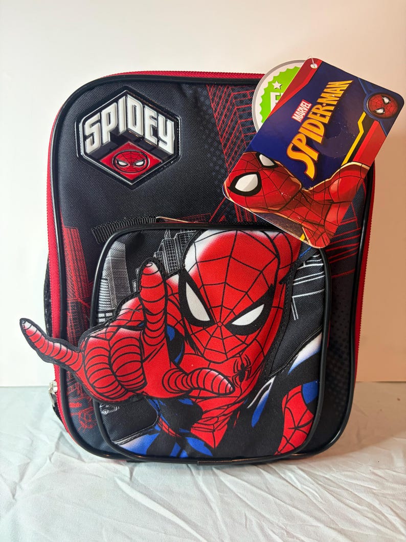 May include: Black and red Spidey backpack featuring a large Spider-Man graphic with outstretched hand. The backpack has the word "SPIDEY" on the top and a Marvel Spider-Man tag attached. The design includes a cityscape and web patterns.
