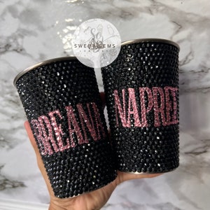 May include: Two black stainless steel tumblers with pink rhinestones spelling out the names "Breann" and "Naphtali".