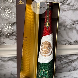 May include: A bottle of 1942 Tequila decorated with rhinestones in the colors of the Mexican flag. The bottle is in a brown box with gold accents.