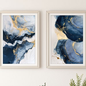 Könnte beinhalten: Zwei gerahmte abstrakte Gemälde mit blauen und goldenen Wirbeln. Die Gemälde sind in weißen Rahmen und hängen an einer weißen Wand.