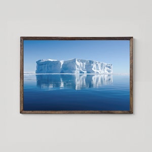 Peut inclure: Une photographie encadrée d'un grand iceberg flottant dans une mer bleue calme. L'iceberg est blanc et se reflète dans l'eau.