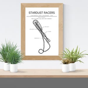 Puede incluir: Una impresión enmarcada con el texto "Stardust Racers" y una ilustración detallada en blanco y negro de una nave espacial. La impresión está en un marco de madera clara y se muestra en una estantería de madera con plantas en macetas.