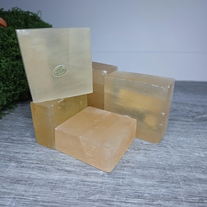 May include: A collection of four translucent, pale yellow, square-shaped blocks of selenite crystal. The blocks are stacked and arranged in a cluster. One block features a small, circular white sticker with the text "MADE IN CHINA" printed on it.