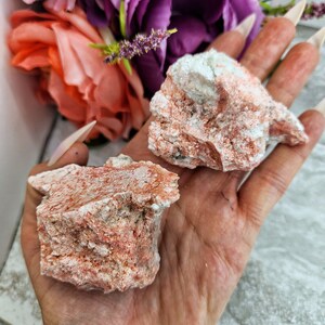 May include: Two rough, natural, orange and white,  crystal clusters. The clusters are irregular in shape and have a rough, textured surface.