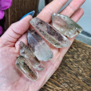 May include: Five clear quartz crystal points with brown and green inclusions. The points are various sizes and shapes.