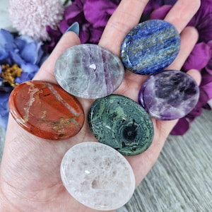May include: Six smooth, oval-shaped polished stones in various colors, including red, green, blue, white, and purple. The stones are arranged in a hand, with the red stone at the bottom and the purple stone at the top.