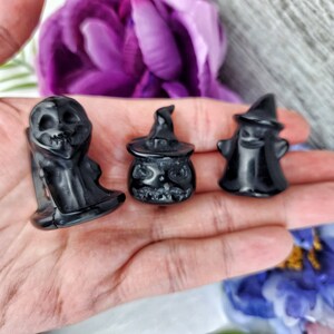 May include: Three black obsidian carvings of Halloween figures: a ghost, a witch, and a pumpkin. The carvings are detailed and have a polished finish.