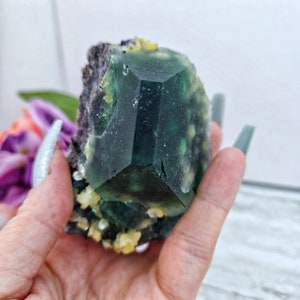 May include: A large green fluorite crystal with yellow inclusions. The crystal is faceted and has a sharp point. It is a beautiful example of this popular mineral.