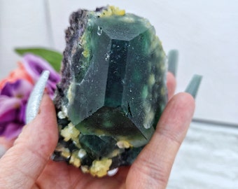 May include: A large green fluorite crystal with yellow inclusions. The crystal is faceted and has a sharp point. It is a beautiful example of this popular mineral.