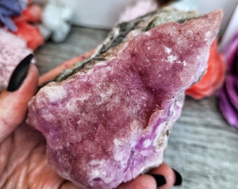 May include: A large, pink and grey crystal with a rough, textured surface. The crystal has a unique, swirling pattern and is a beautiful example of natural beauty.