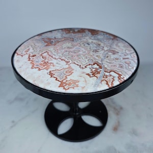 May include: A circular display stand featuring a polished stone top with intricate, swirling patterns in shades of white, cream, and reddish-brown. The stand is supported by a black metal base with a central post and a circular, cutout design.
