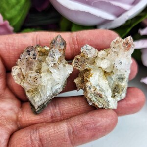 May include: Two clusters of clear quartz crystals with brown and black inclusions. The crystals are clustered together in a natural formation.