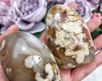 May include: Two polished agate stones with a white, brown, and gray color pattern. The stones are smooth and have a natural, organic shape.