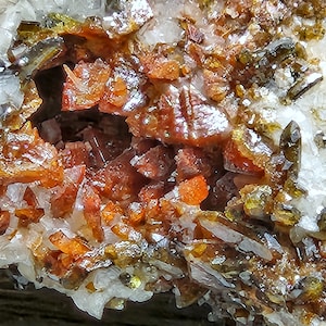 May include: Close-up of a cluster of red and orange crystals with a glassy sheen. The crystals are embedded in a matrix of white and green crystals.