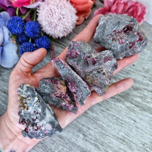 May include: A collection of raw pink and gray crystals. The crystals are rough and have a natural, unpolished look. They are a beautiful example of the natural beauty of crystals.