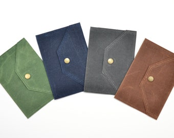 Puede incluir: Cuatro sobres de tela en diferentes colores: verde, azul, gris y marrón. Cada sobre tiene una solapa con un solo botón de latón.