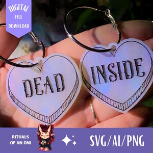 May include: Two iridescent heart-shaped earrings with black text. The earrings say "DEAD" and "INSIDE".