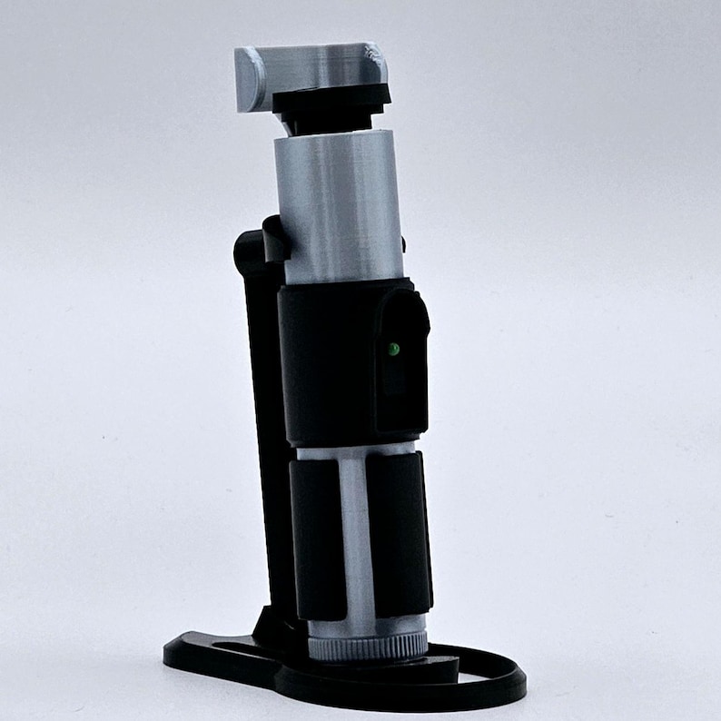 May include: A 3D printed lightsaber prop with a black handle and a silver blade. The lightsaber is on a black stand.