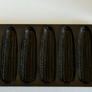 May include: Black cast iron cornbread pan with eight individual moulds shaped like corn cobs.