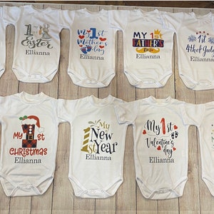 May include: Twelve white baby onesies with different holiday themes, each with the text "My 1st" and the name "Ellianna".