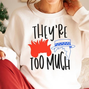 May include: White sweatshirt with a red and blue graphic of two cartoon characters and the text "They're Too Much".