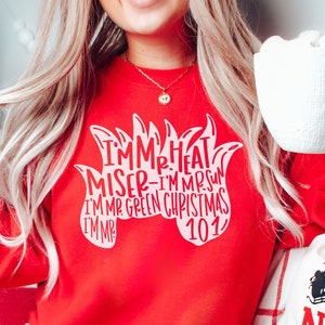 May include: Red sweatshirt with white text that reads "I'm Mr. Heat Miser - I'm Mr. Sun - I'm Mr. Green Christmas 101".