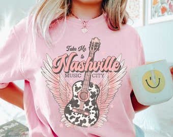 May include: Pink t-shirt with a graphic of a guitar with wings and the text "Take Me to Nashville Music City".