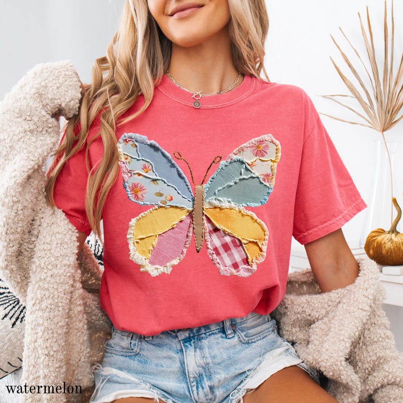 May include: A watermelon-colored t-shirt features a patchwork butterfly design. The butterfly's wings are composed of various fabric patterns, including floral, gingham, and solid colors. The shirt has a relaxed fit and short sleeves. The word "watermelon" is printed at the bottom left.