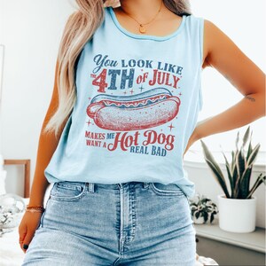 Puede incluir: Camiseta sin mangas azul claro con un gr&aacute;fico que dice "You look like the 4th of July makes me want a hot dog real bad." El gr&aacute;fico presenta una ilustraci&oacute;n de perrito caliente rojo y azul. La camiseta sin mangas es sin mangas.